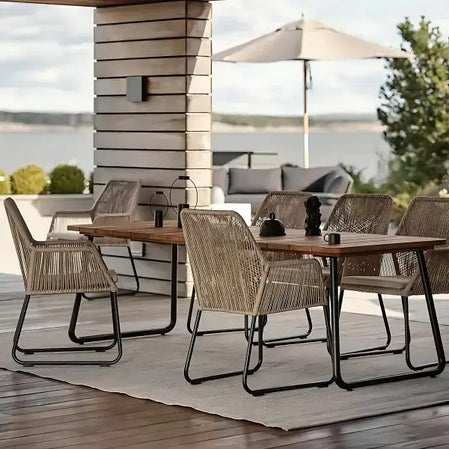 Udendørs spisebordssæt i skandinavisk design med flettede havestole og sort metalramme, placeret på en terrasse med udsigt over en sø. Perfekte havemøbler til dansk sommer, ideelle til hyggelige udendørs middage og som en del af moderne terrasseindretning.